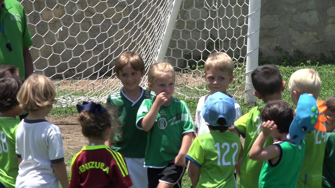 Children in soccer jerseys gathered near a goal net.