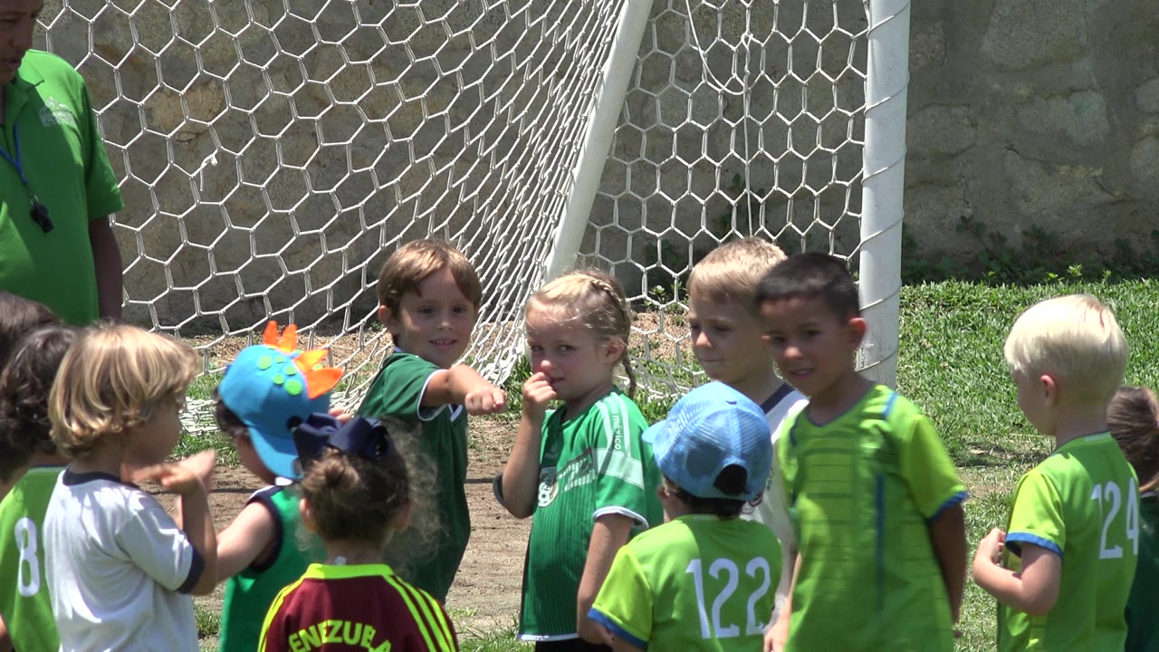 Children in football shirts gather beside a goal net.