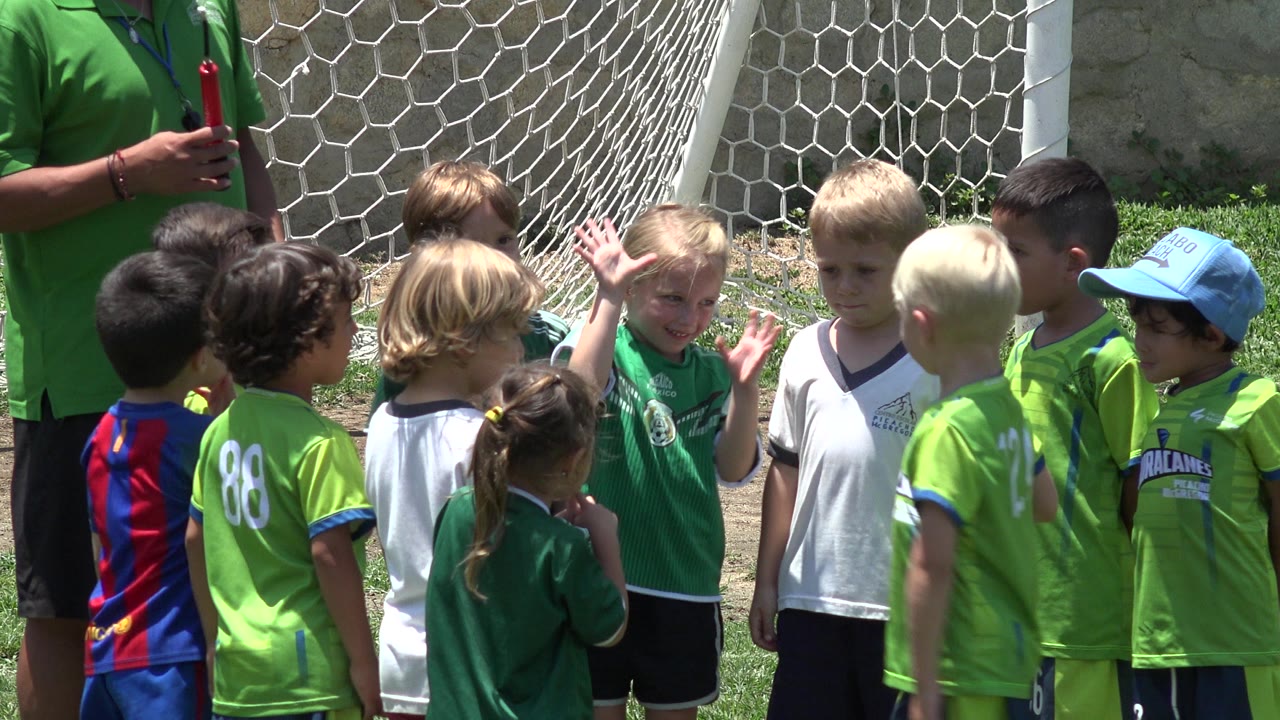Children in soccer jerseys gathered by a goal net with a coach partly visible.