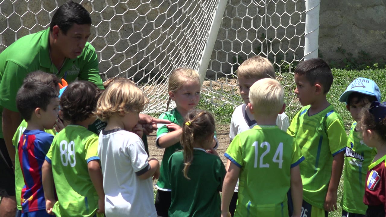 The group of children remains gathered in front of the white soccer net in Cabo San Lucas, Mexico, with jersey numbers visible on their backs.