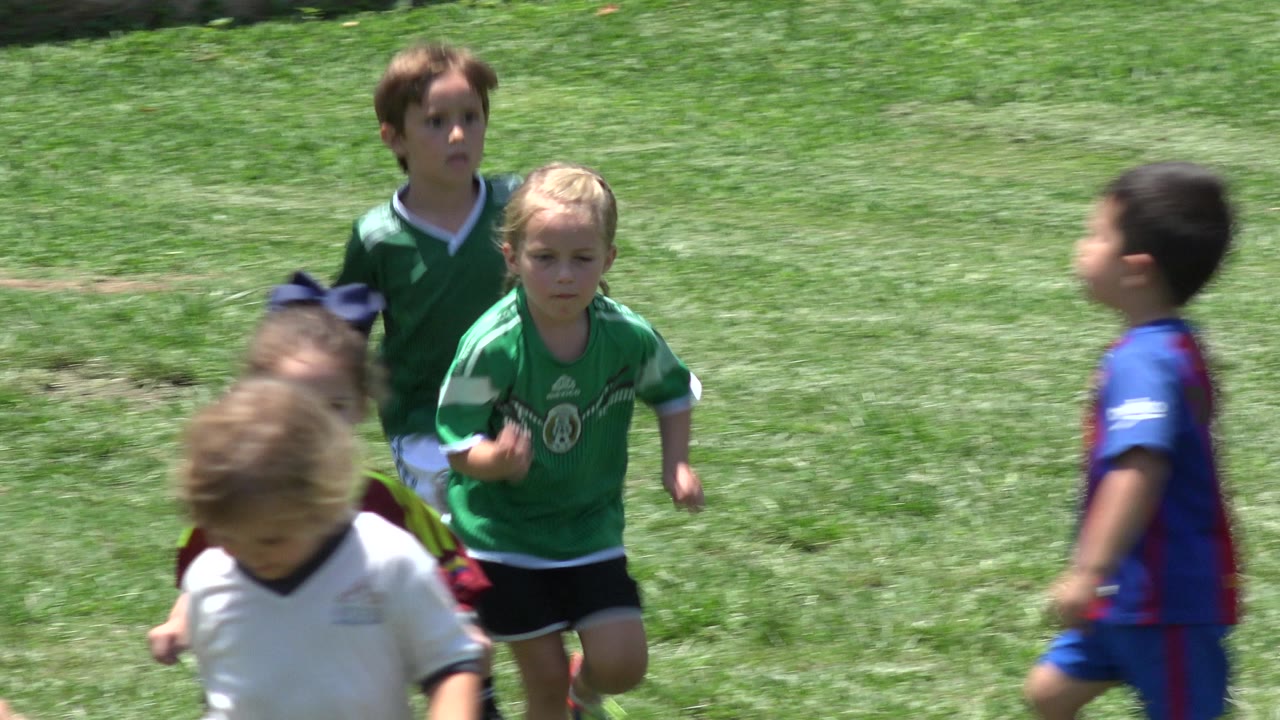 Children running on a sunny grass field in soccer jerseys.