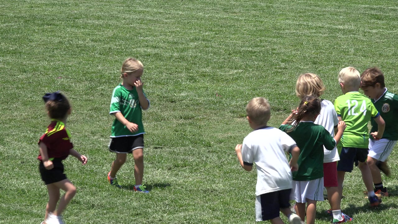 Children in soccer shirts standing and running on a grass field.
