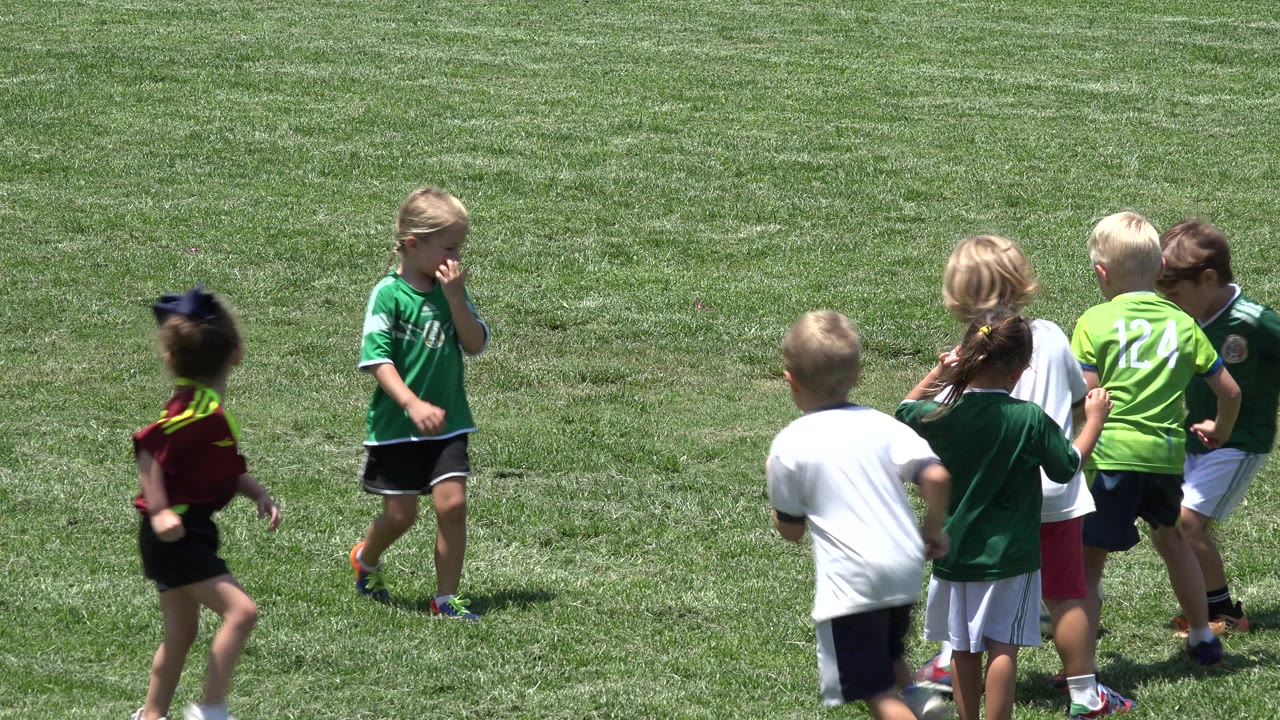 Several young players stand close together on the green field in Cabo San Lucas, Mexico, with one child in a bright green jersey facing away.
