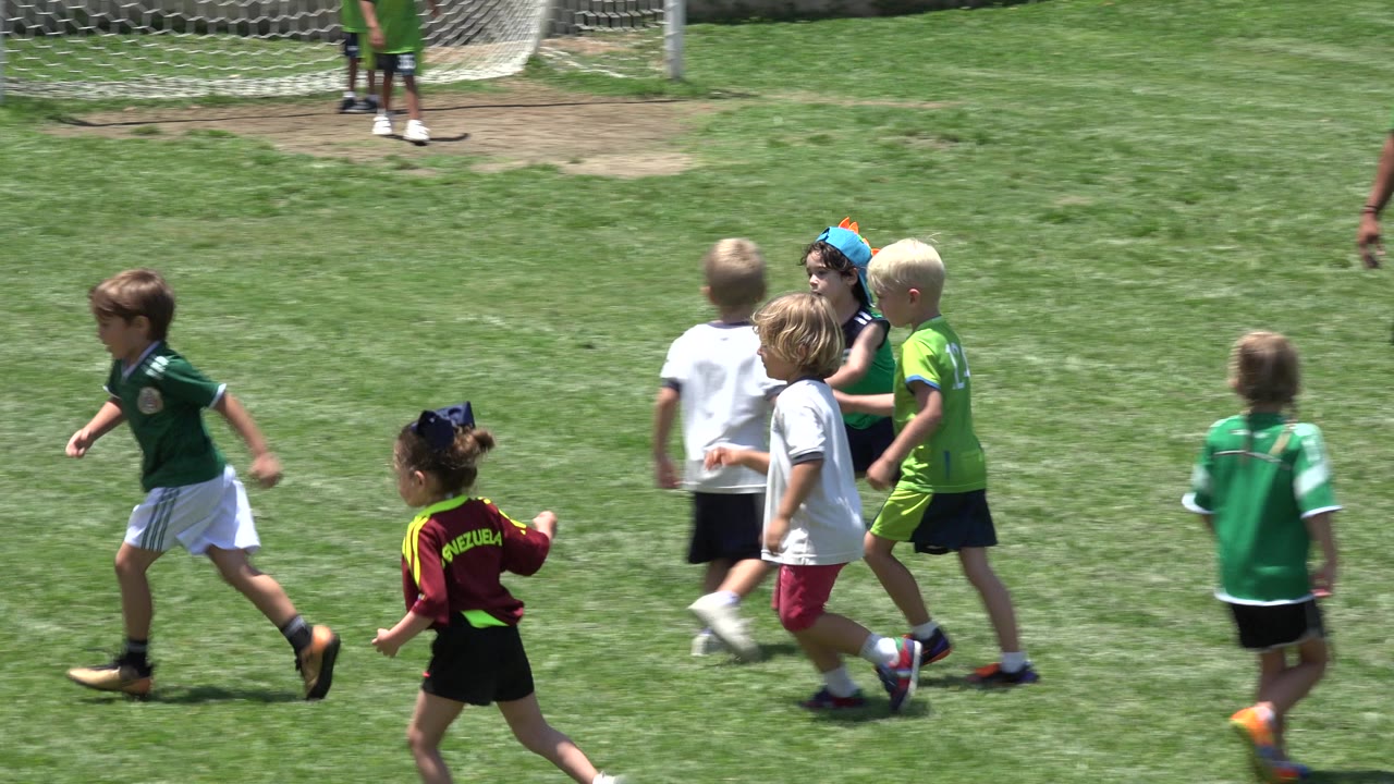 Several young players in green, white, lime, and maroon jerseys move across the Cabo San Lucas soccer field under strong sun.