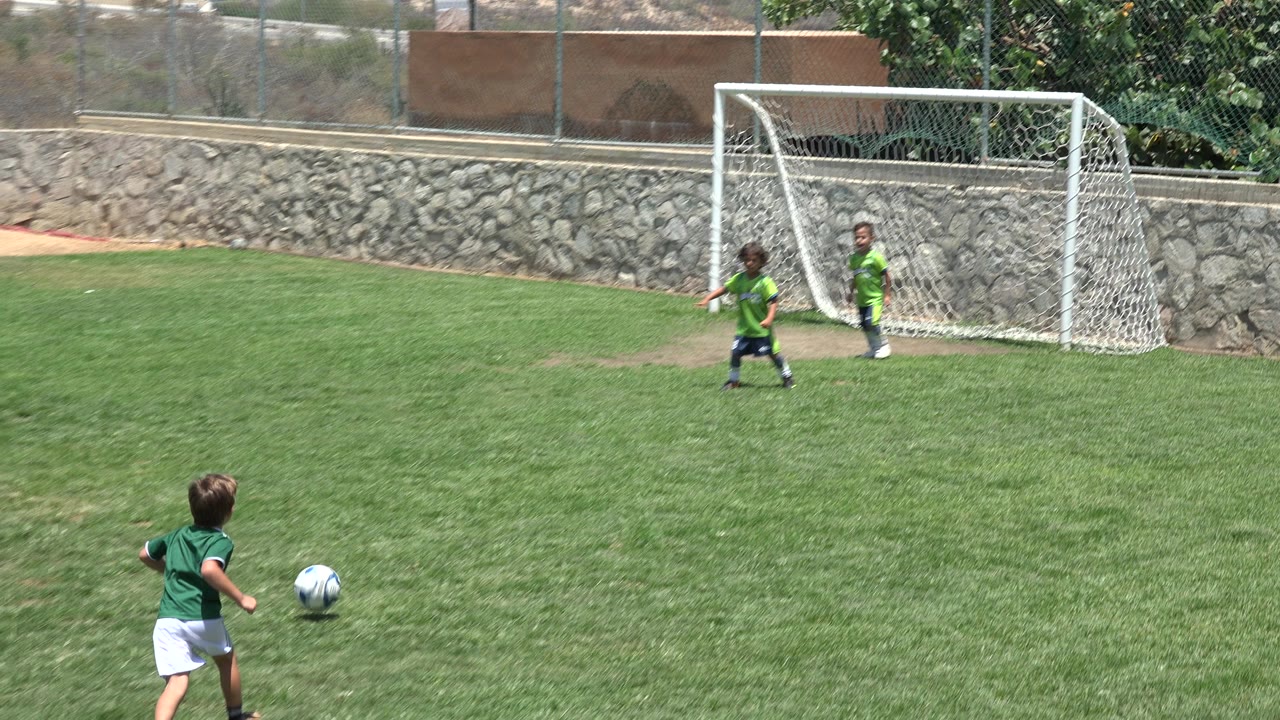 At 0:01 in Cabo San Lucas, Mexico, the ball rolls ahead of a running child while two young players remain beside the white goal and net.