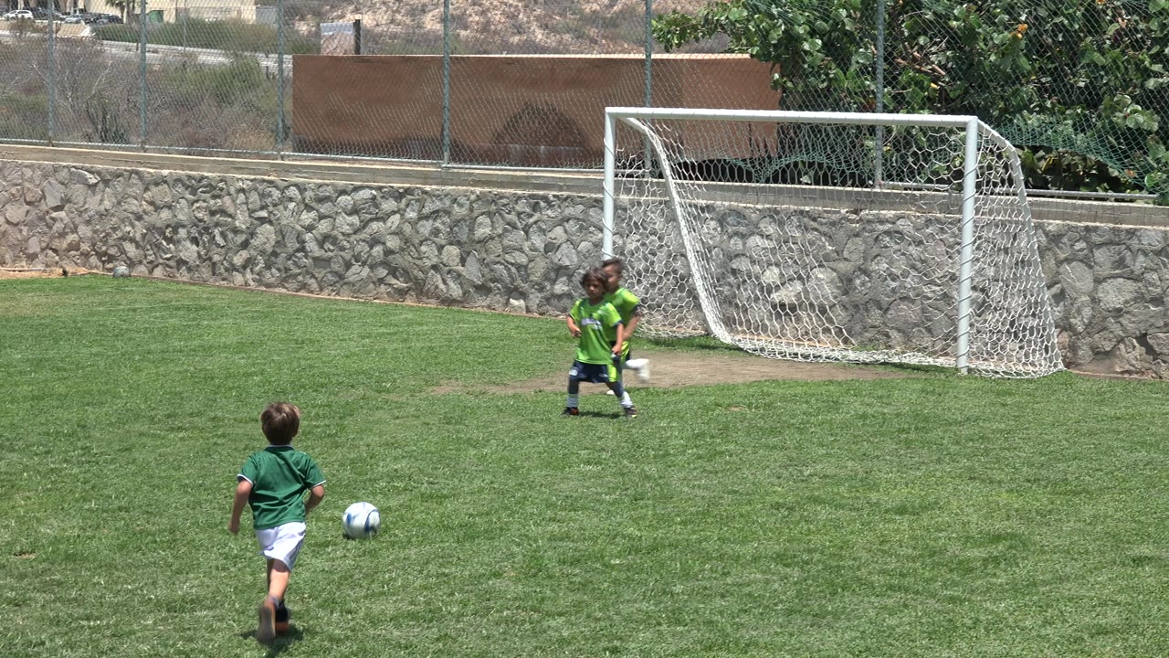 Young player runs toward the goal with a soccer ball ahead on the grass.