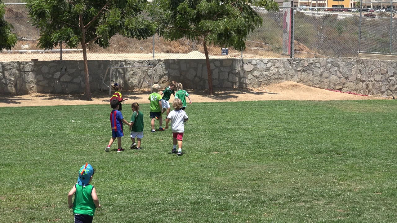 Small group of children gather near the soccer ball on grass.