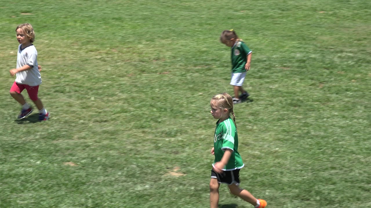 A girl in a green jersey crosses the foreground while other children run behind her on the open soccer field in Cabo San Lucas, Mexico.