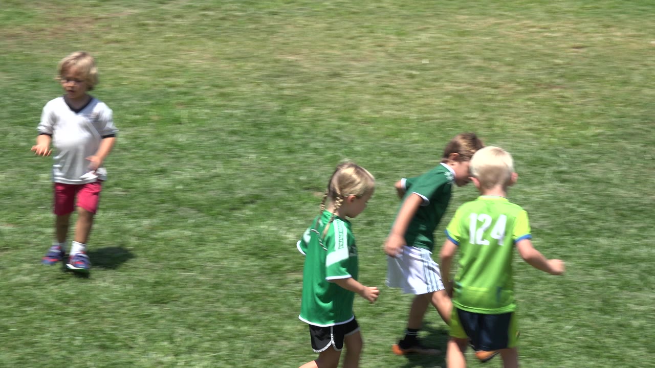 A blond child in a bright green jersey moves beside other children in green and white shirts on the Cabo San Lucas grass field.