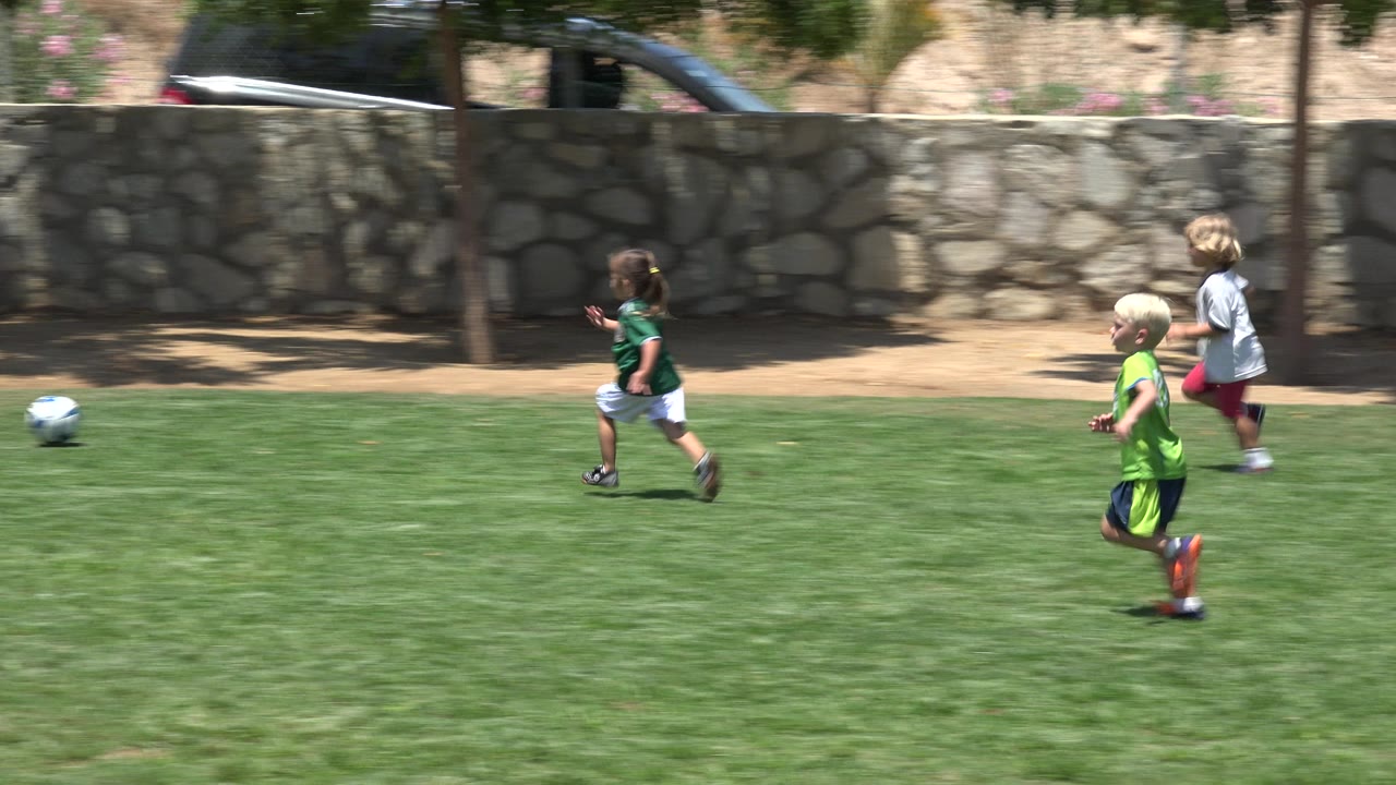 Children running on a grass field near a soccer ball