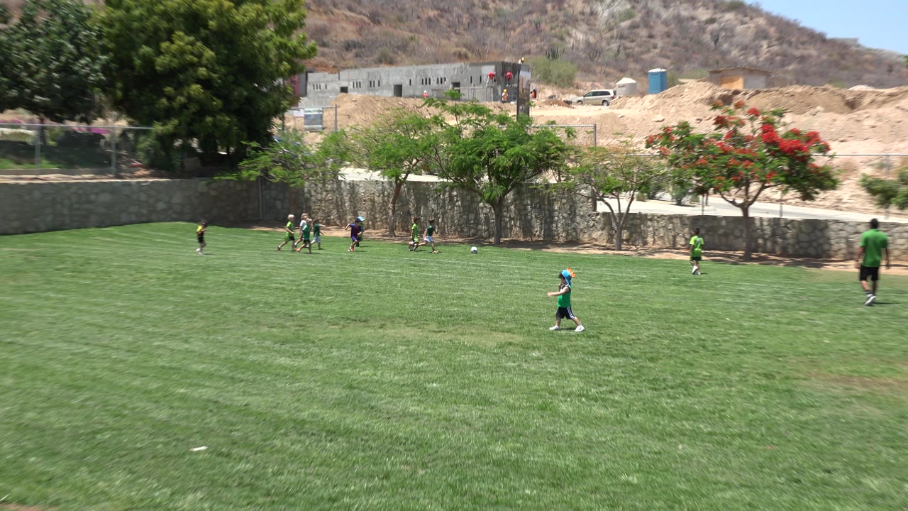 Children continue playing soccer across a green field.