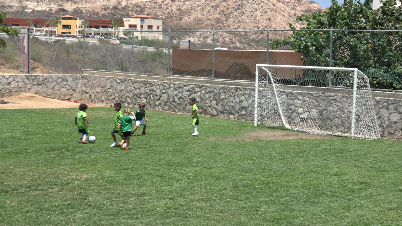 Children cluster around a soccer ball near the goal mouth.