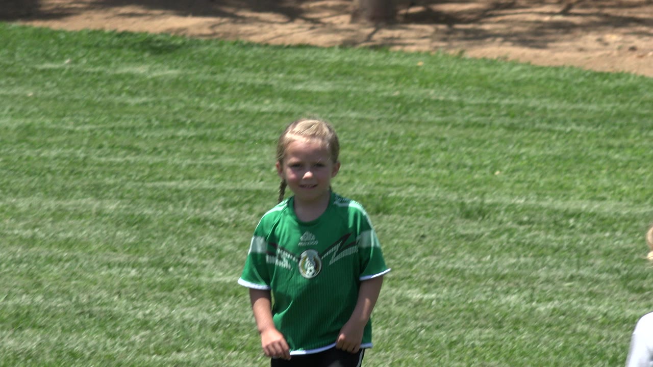 The green-jersey child remains near center on the Cabo San Lucas lawn while part of another child in a white shirt appears at the lower edge.