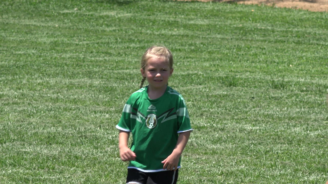 Child in green jersey on a sunlit grass field.