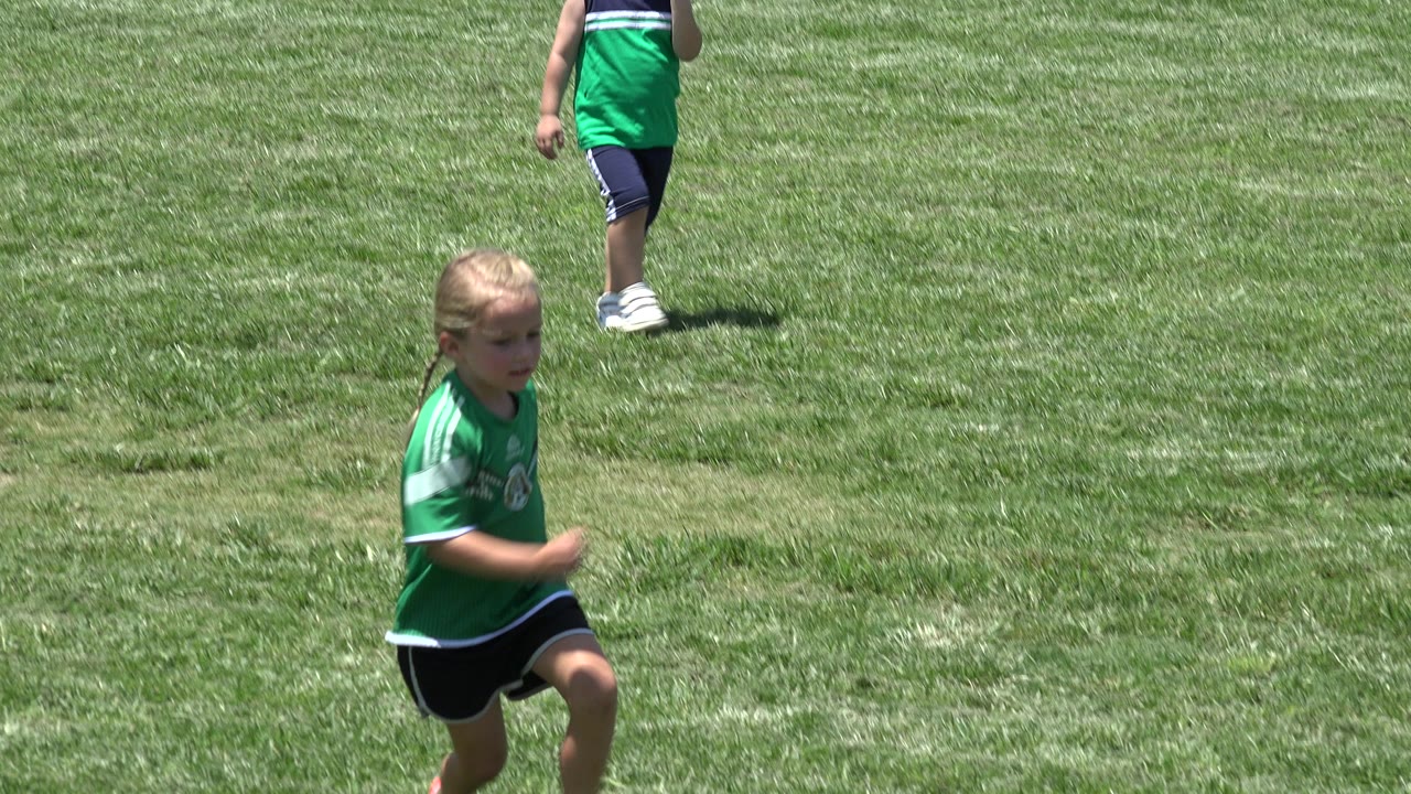 The girl continues running over the green field in Cabo San Lucas, Mexico, while a background child is cropped at the top of the frame.