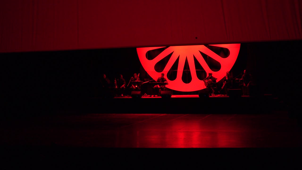 Dark stage with red fan-shaped backdrop and curtain partly lowered.