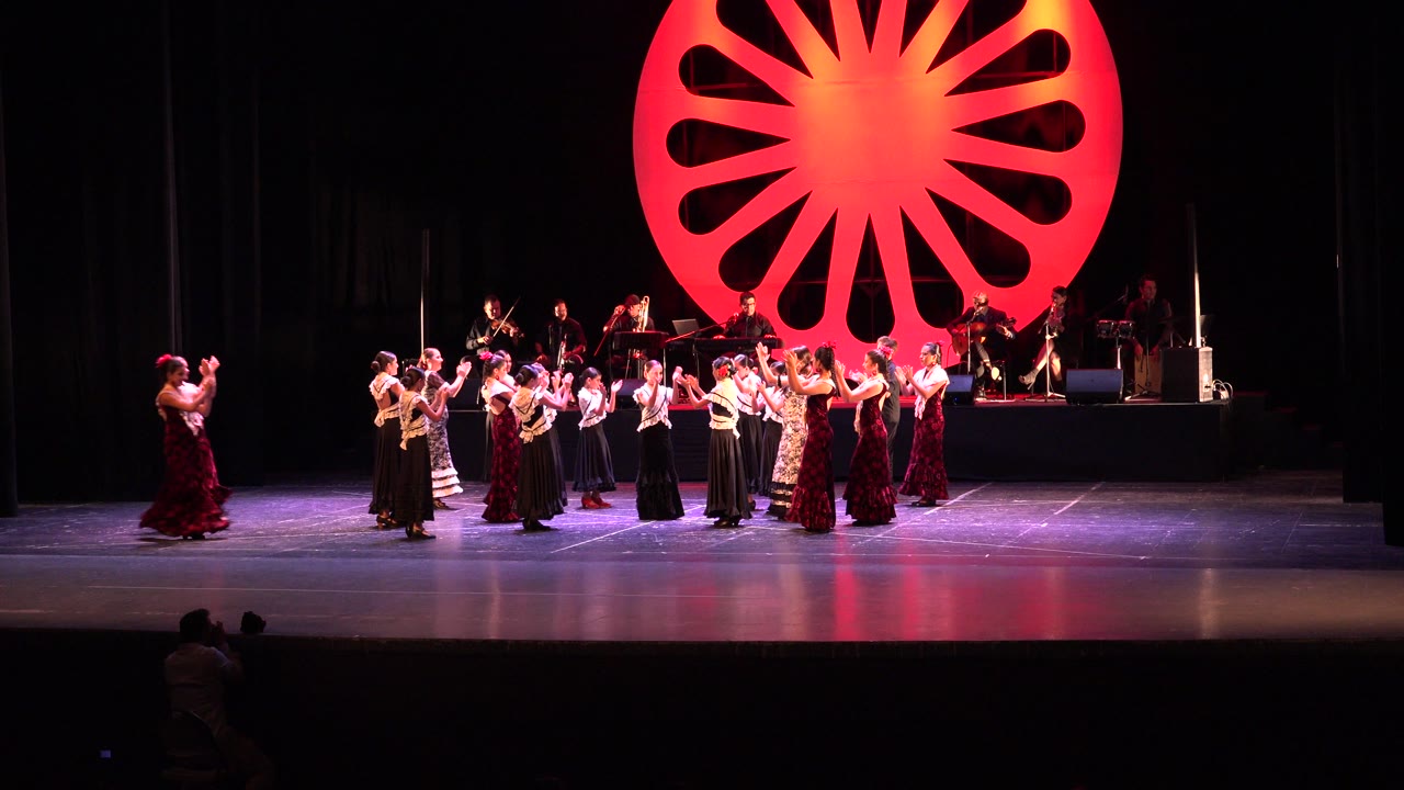 Wide theater stage with children dancing in front of a red circular backdrop