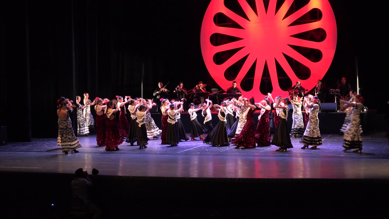 Cabo San Lucas performance frame with dancers holding raised arm positions across the lit stage while musicians remain visible behind the group.