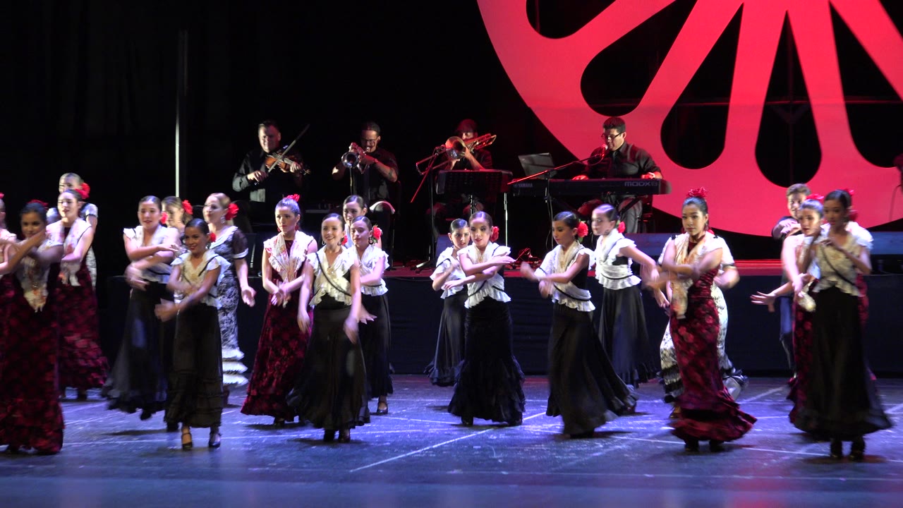 Wide stage view of young dancers performing with musicians behind them.