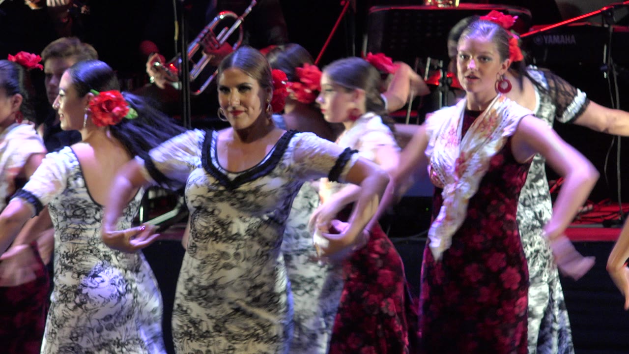 Dancers cluster near center stage with arms lifted and musicians in back.