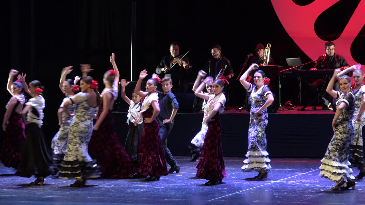Women in long dresses dancing on a stage with musicians behind them.