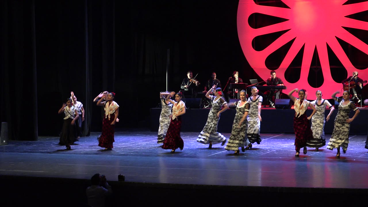 Dancers in dresses and shawls perform across a theater stage