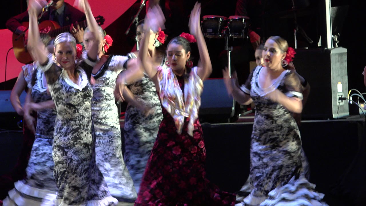 Women dancing on a stage with musicians behind them.