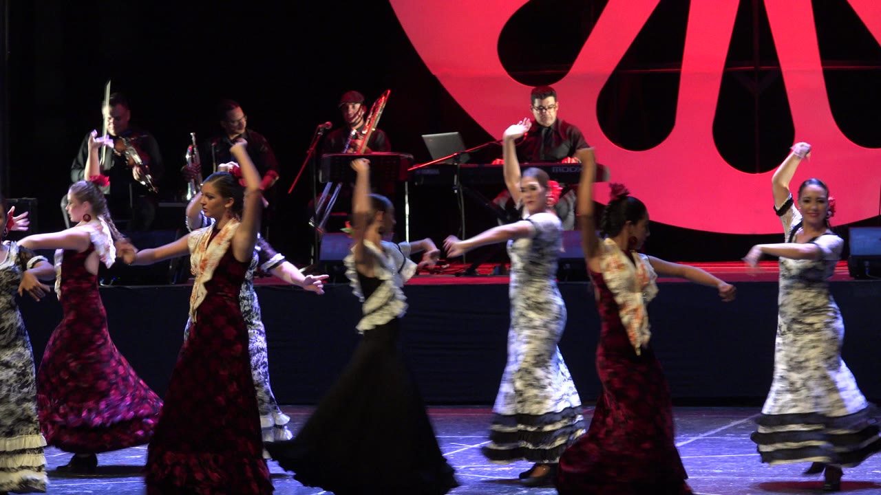 Dancers perform on stage in front of musicians and a red backdrop.