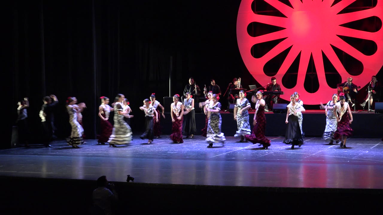 Wide stage view of flamenco dancers and musicians under red lighting.