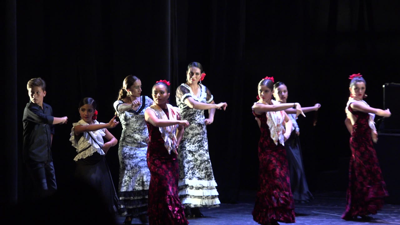 Group of dancers on a dark stage with arms extended.