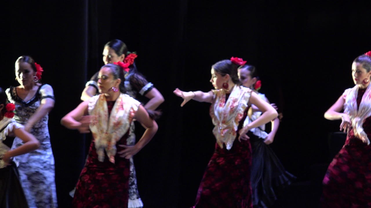 Women in red and black dance costumes performing on a dark stage.