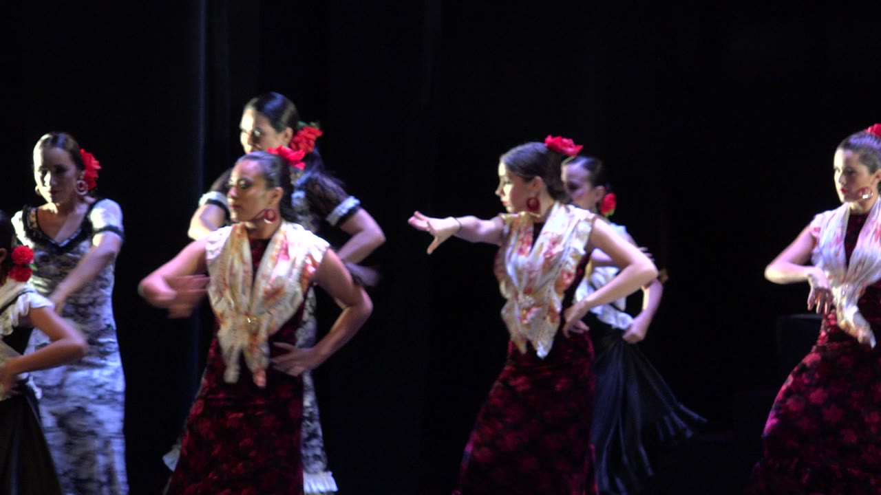 A lead dancer in a red patterned skirt extends her arm while other costumed women perform behind her on a Cabo San Lucas stage.