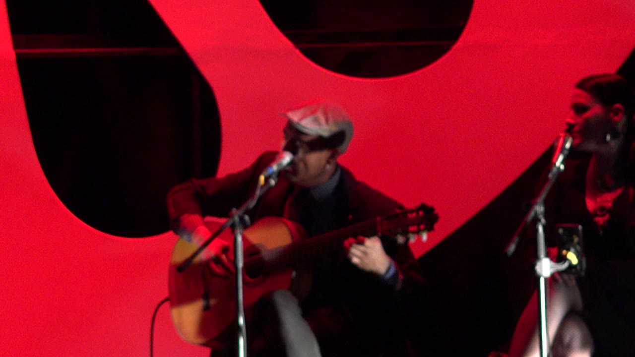 At 0:01 in Cabo San Lucas, the guitarist remains centered with his hand on the guitar neck while the woman at the right microphone is visible in profile.