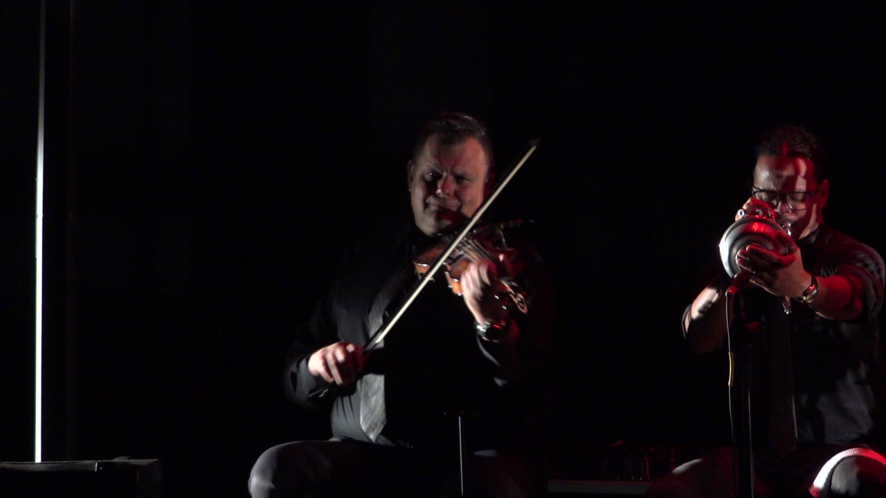 One second in, the Cabo San Lucas stage view holds on the violinist at left and trumpet player at right, with the trumpet catching a stronger red highlight.