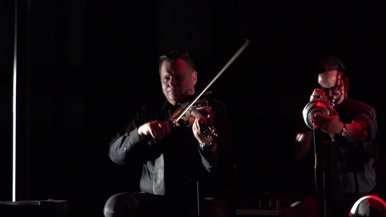 Violinist and trumpet player performing in a dark room.