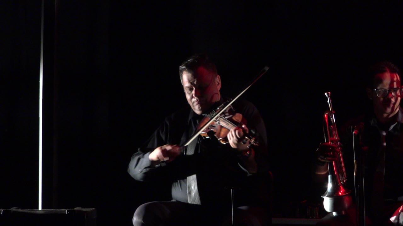 Violinist playing beside a dimly lit trumpet player