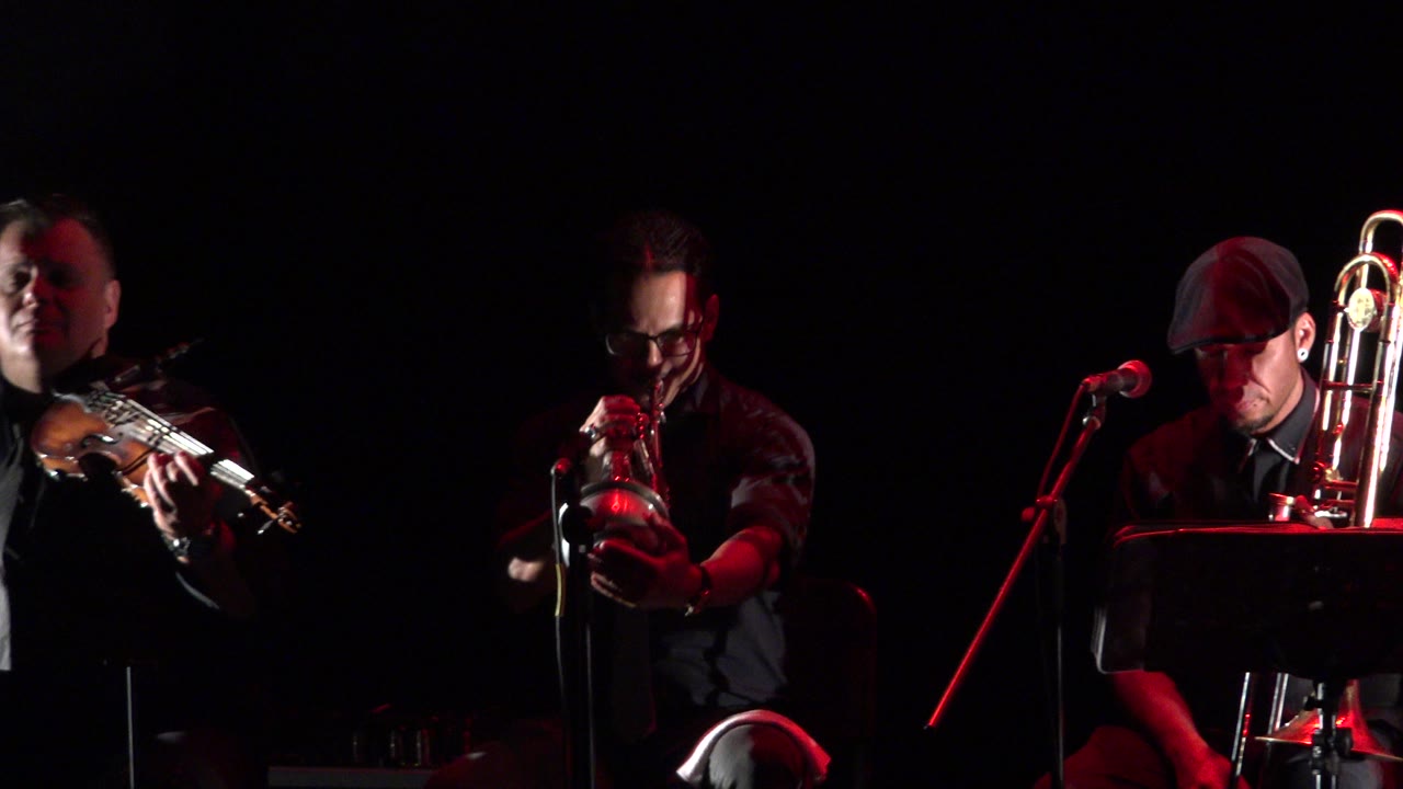 Stage musicians playing violin and trumpet under red light.
