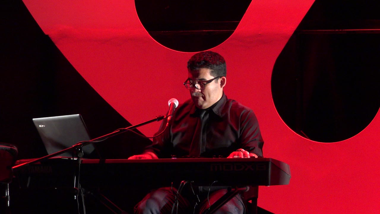 Man at keyboard beside a microphone on a red-lit stage.