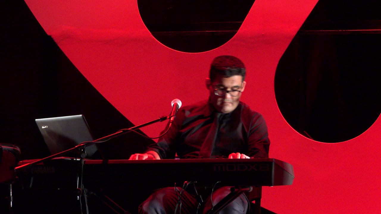 In Cabo San Lucas, Mexico, the keyboard player looks down at the keys while the microphone points toward him and the laptop remains open on the left.