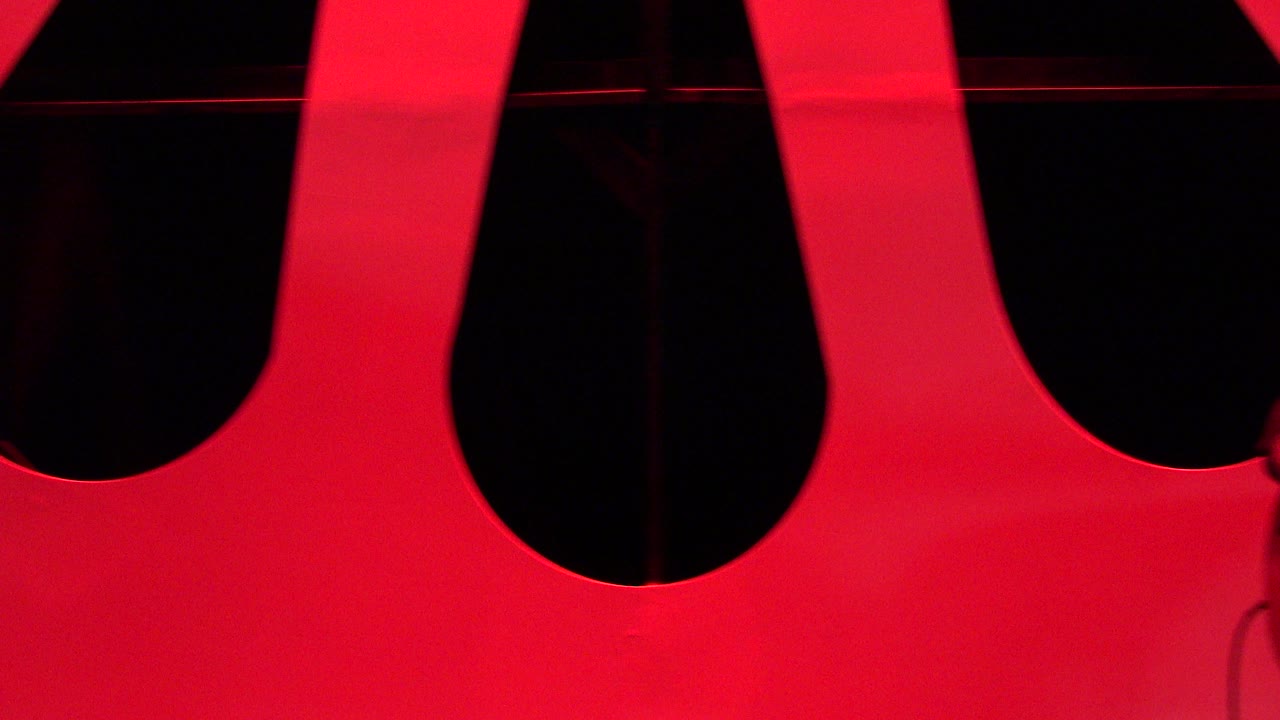 Opening frame in Cabo San Lucas shows only a large red stage backdrop with black cutout shapes and no visible people.