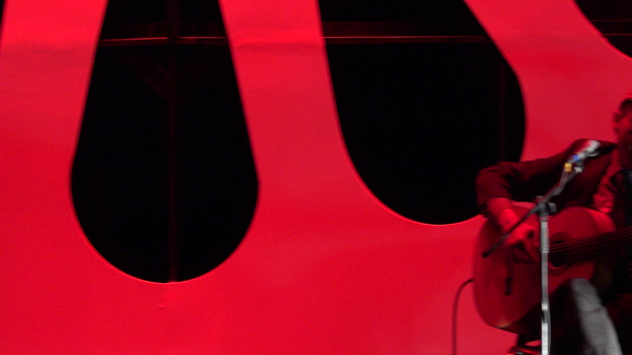 Partial guitarist entering frame at the right edge near a microphone.