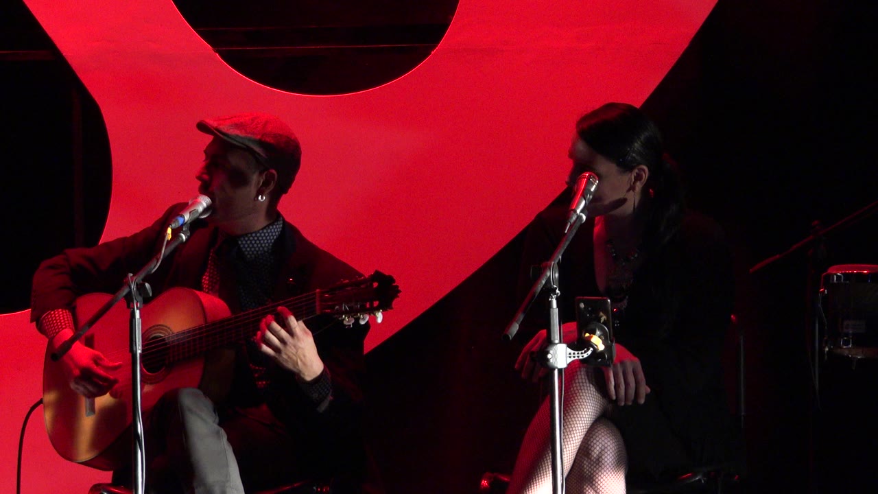 Seated guitarist and singer under red stage lighting.