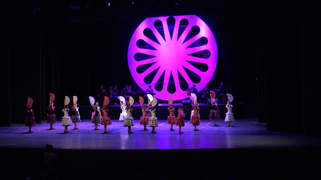 Closer stage view of girls in colorful costumes lined up while dancing.