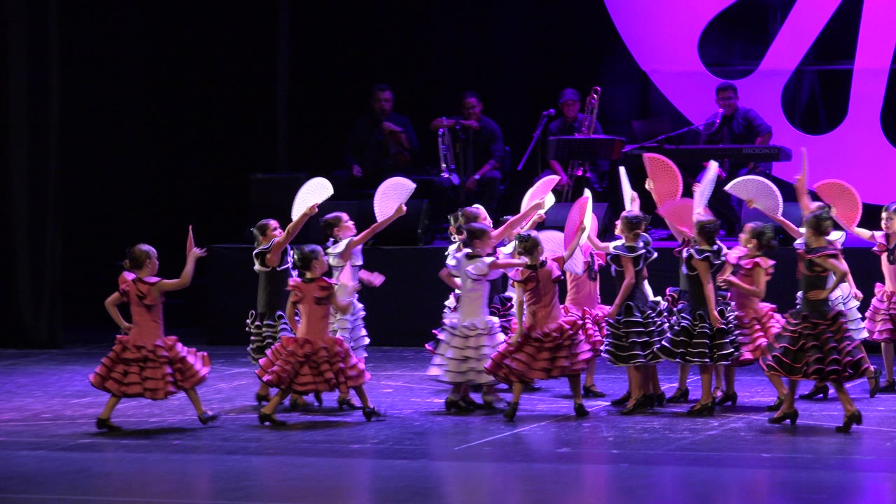 Group of girls clusters with fans raised on stage.