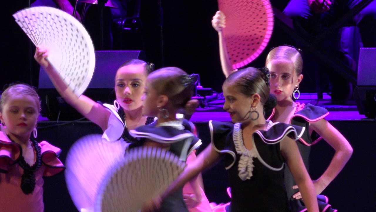 Girls in black, pink, and white costumes hold folding fans on a purple-lit stage.
