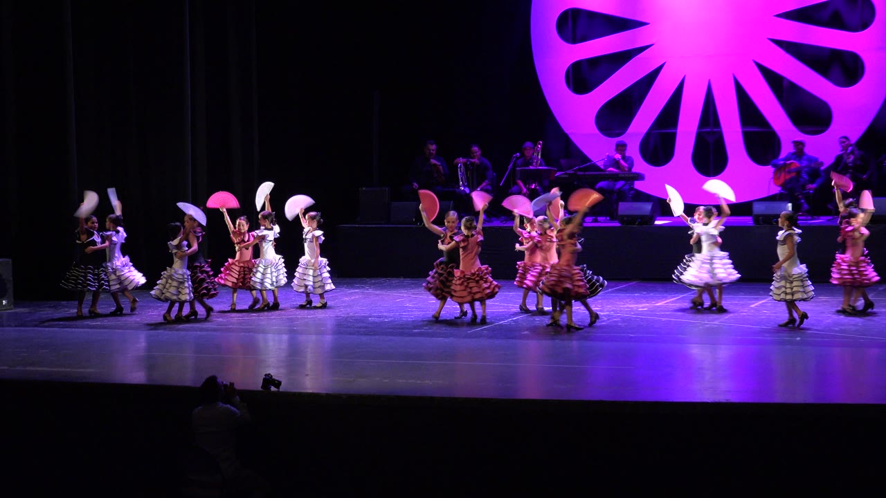 Children dance with folding fans on a purple-lit stage.