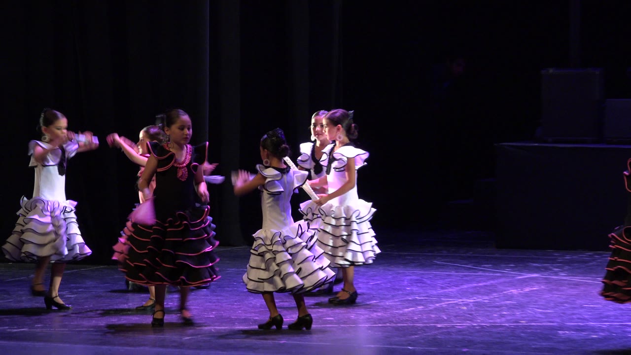 Young girls in black, white, and pink ruffled dance costumes perform together on a dark stage in Cabo San Lucas, Mexico.