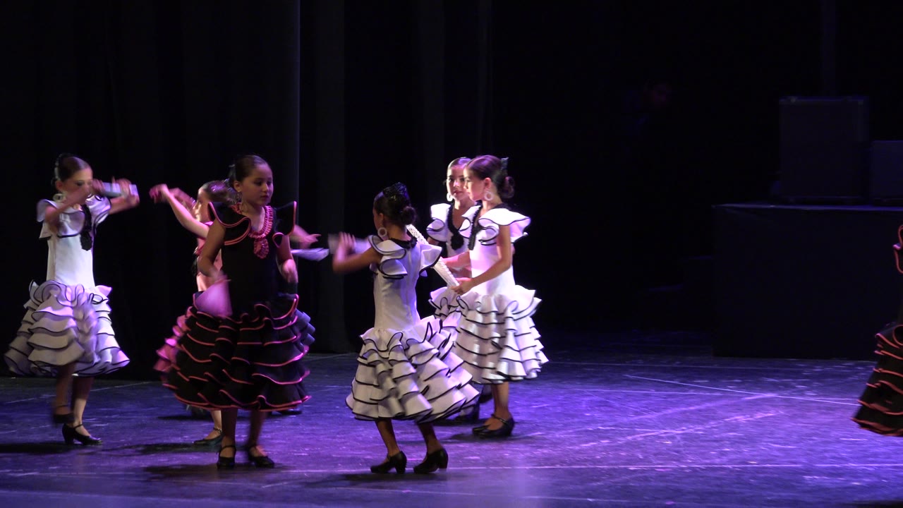 Several young girls continue the routine on a purple-lit stage in Cabo San Lucas, with two dancers facing inward and arms extended.