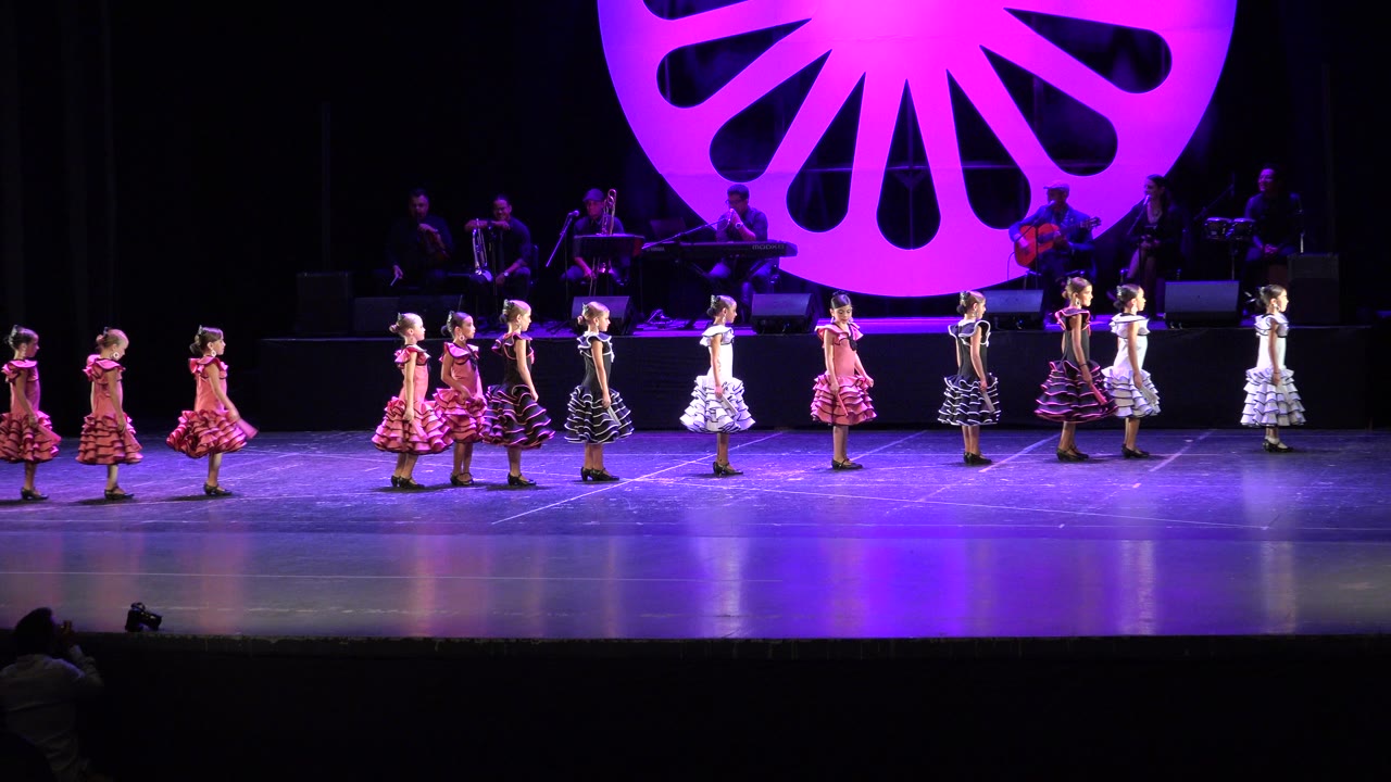 Girls in ruffled dresses line up on a purple-lit stage.