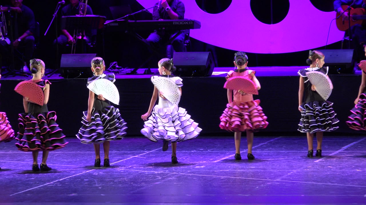 Dancers turn with fans on a stage under purple lighting.